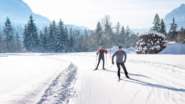 Zwei Langläufer auf schneebedeckter Loipe vor verschneiten Bergen