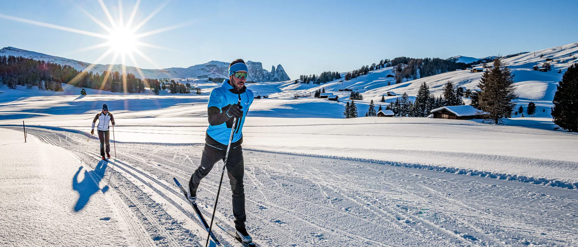 Two people cross-country skiing on a snowy trail in clear weather