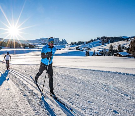 Two people cross-country skiing on a snowy trail in clear weather