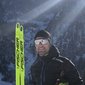 Man in winter sports outfit with skis in front of snowy mountains in sunlight