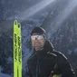 Mann im Wintersport-Outfit mit Skiern vor schneebedeckten Bergen im Sonnenschein