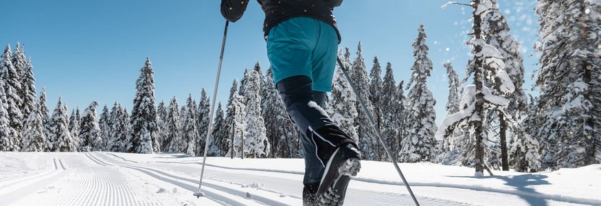 Person beim Langlaufen auf sonniger, verschneiter Strecke mit blauen Himmel