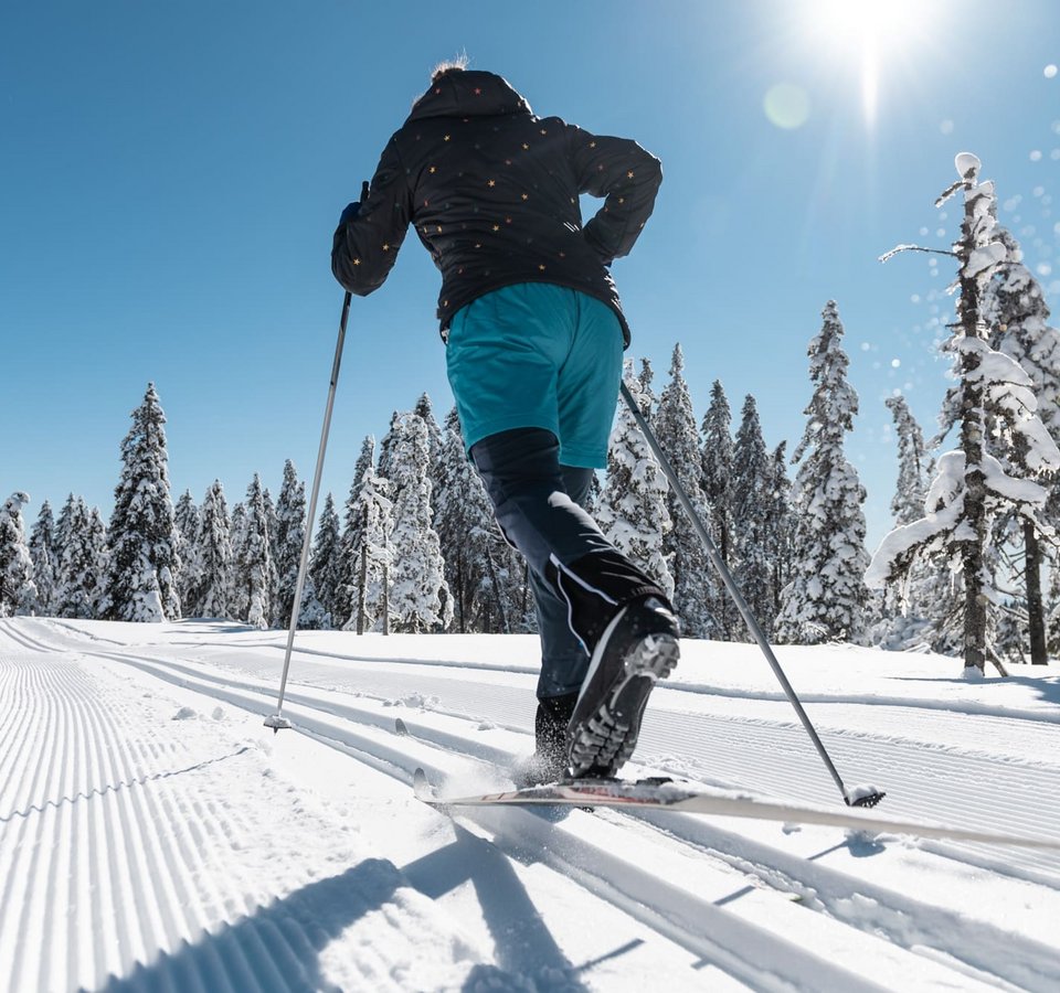 Person beim Langlaufen auf sonniger, verschneiter Strecke mit blauen Himmel