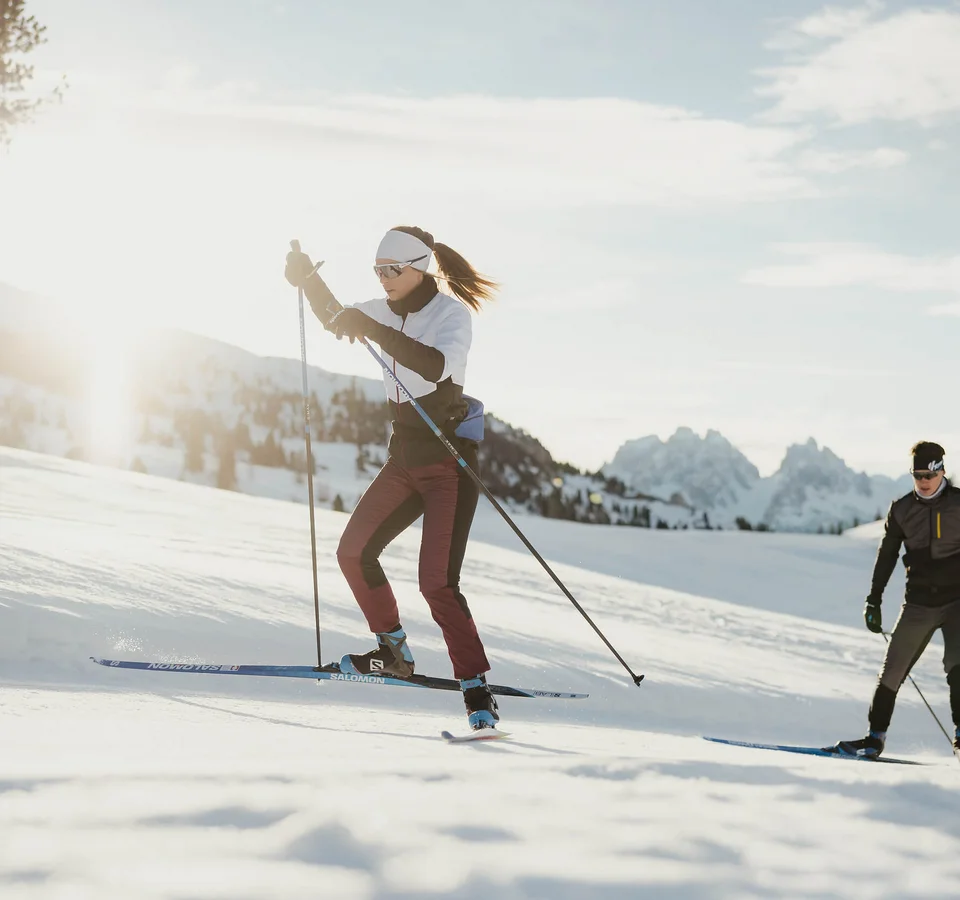 Zwei Personen Langlauf im Schnee mit Bergen im Hintergrund