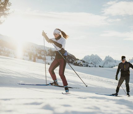 Zwei Personen Langlauf im Schnee mit Bergen im Hintergrund