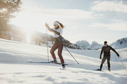 Zwei Personen Langlauf im Schnee mit Bergen im Hintergrund