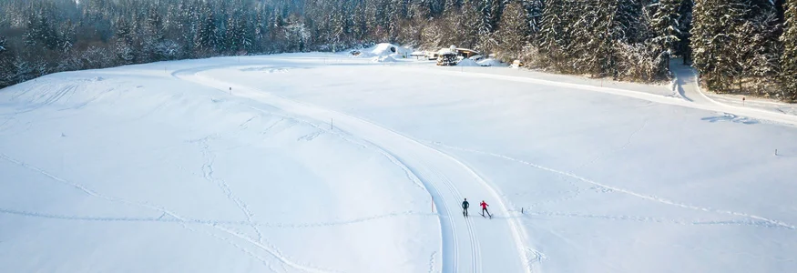 Die Kaiserwinklloipe © Tourismusverband Kaiserwinkl Zwei Skifahrer auf verschneiter Loipe vor verschneiten Bergen und Wald