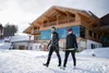 Sammelanfragen © Fabian Dalpiaz Zwei Skifahrer tragen Langlaufskier vor einem Chalet im Schnee
