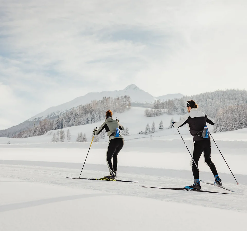Two people cross-country skiing in snowy mountain landscape