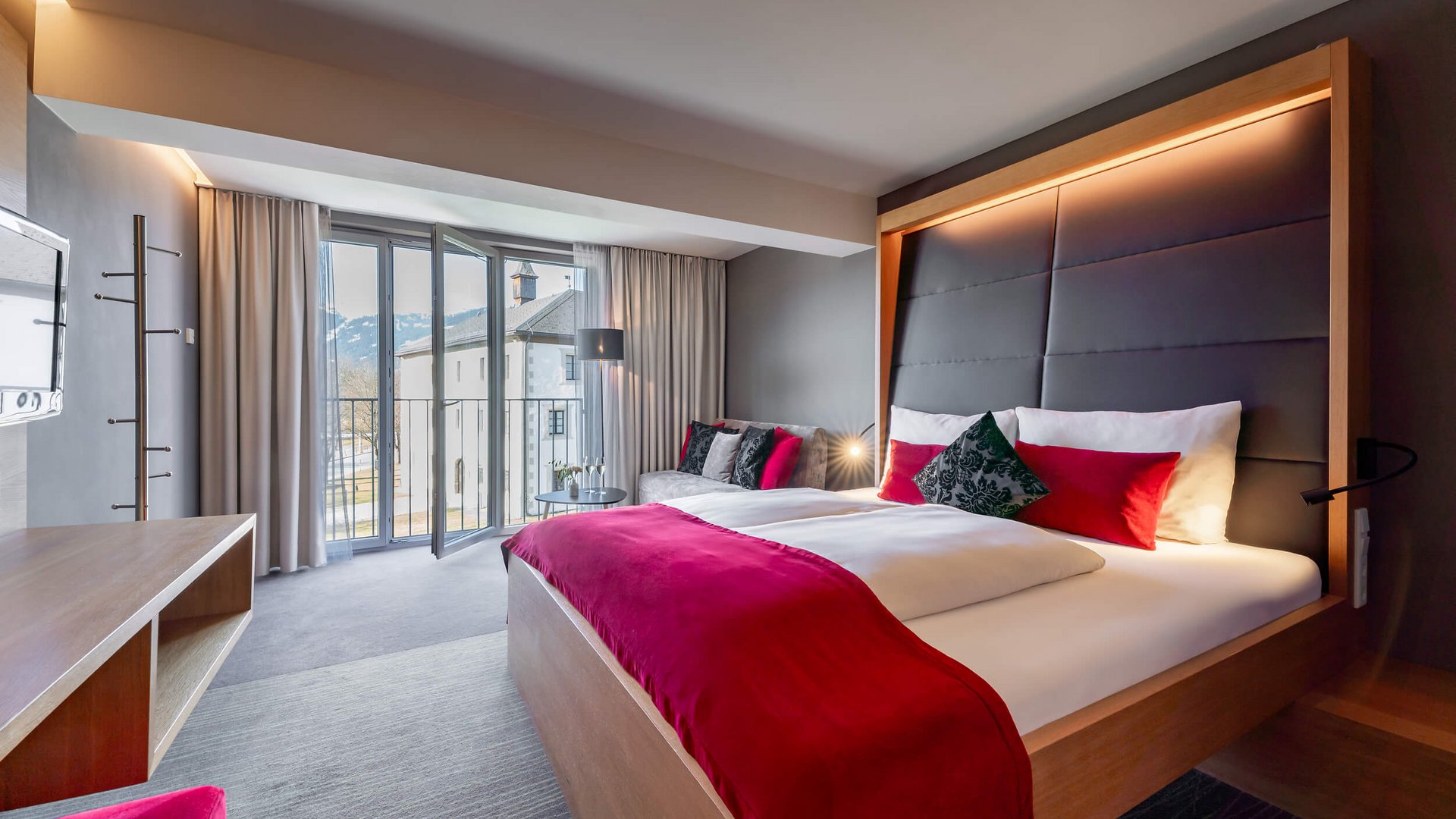 Modern hotel room with large bed and open balcony door showing mountain view