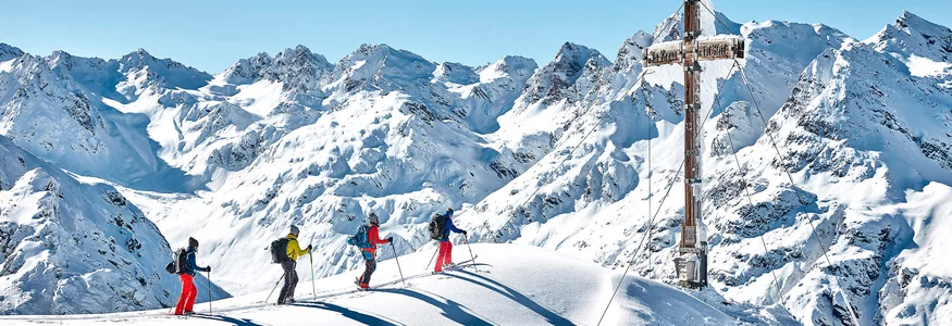 Four skiers on snowy peak near large summit cross