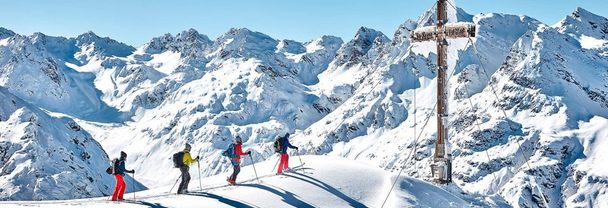 Four skiers on snowy peak near large summit cross