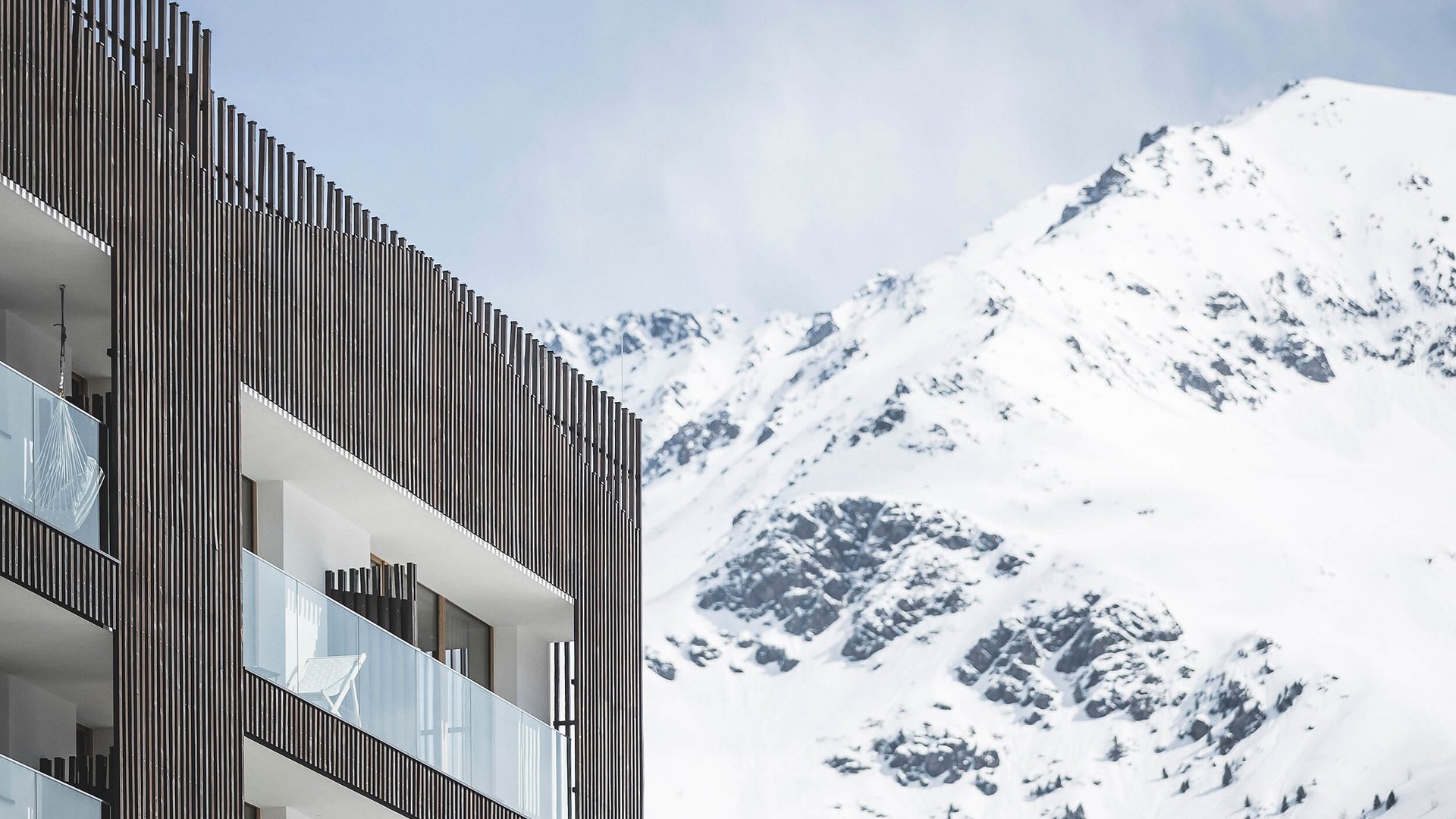 Moderner Balkon mit Glasgeländern vor verschneitem Bergpanorama