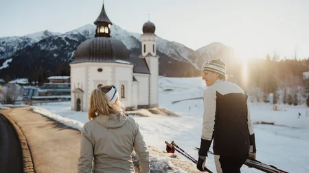 Schneesicher langlaufen: Wo Snowfarming in Österreich frühen Saisonstart möglich macht
© Alex Moling Zwei Langläufer im Winter vor einer Kirche in den Bergen bei Sonnenuntergang