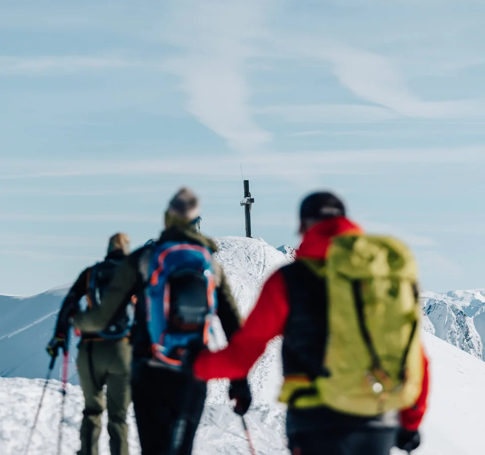 Skitouren-Kurse im Passeiertal © Tourismusverein Passeiertal - Benjamin Pfitscher Wanderer auf schneebedecktem Bergweg im Winter, Gipfelkreuz sichtbar