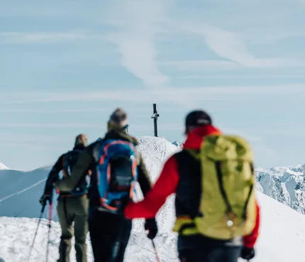 Wanderer auf schneebedecktem Bergweg im Winter, Gipfelkreuz sichtbar