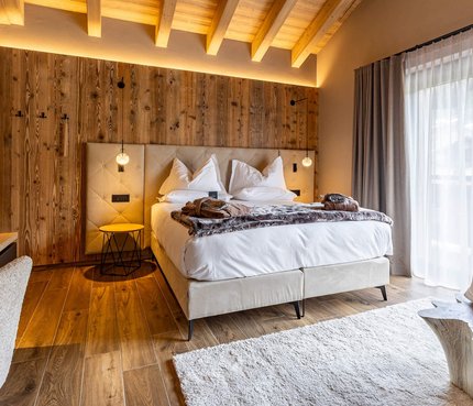 Gemütliches Hotelzimmer mit Holzwand, Doppelbett und großem Fenster