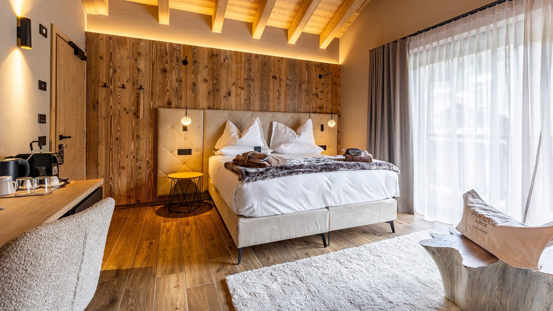 Gemütliches Hotelzimmer mit Holzwand, Doppelbett und großem Fenster