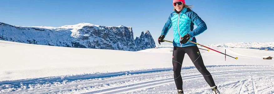 Frau beim Langlauf vor verschneiten Bergen und blauem Himmel