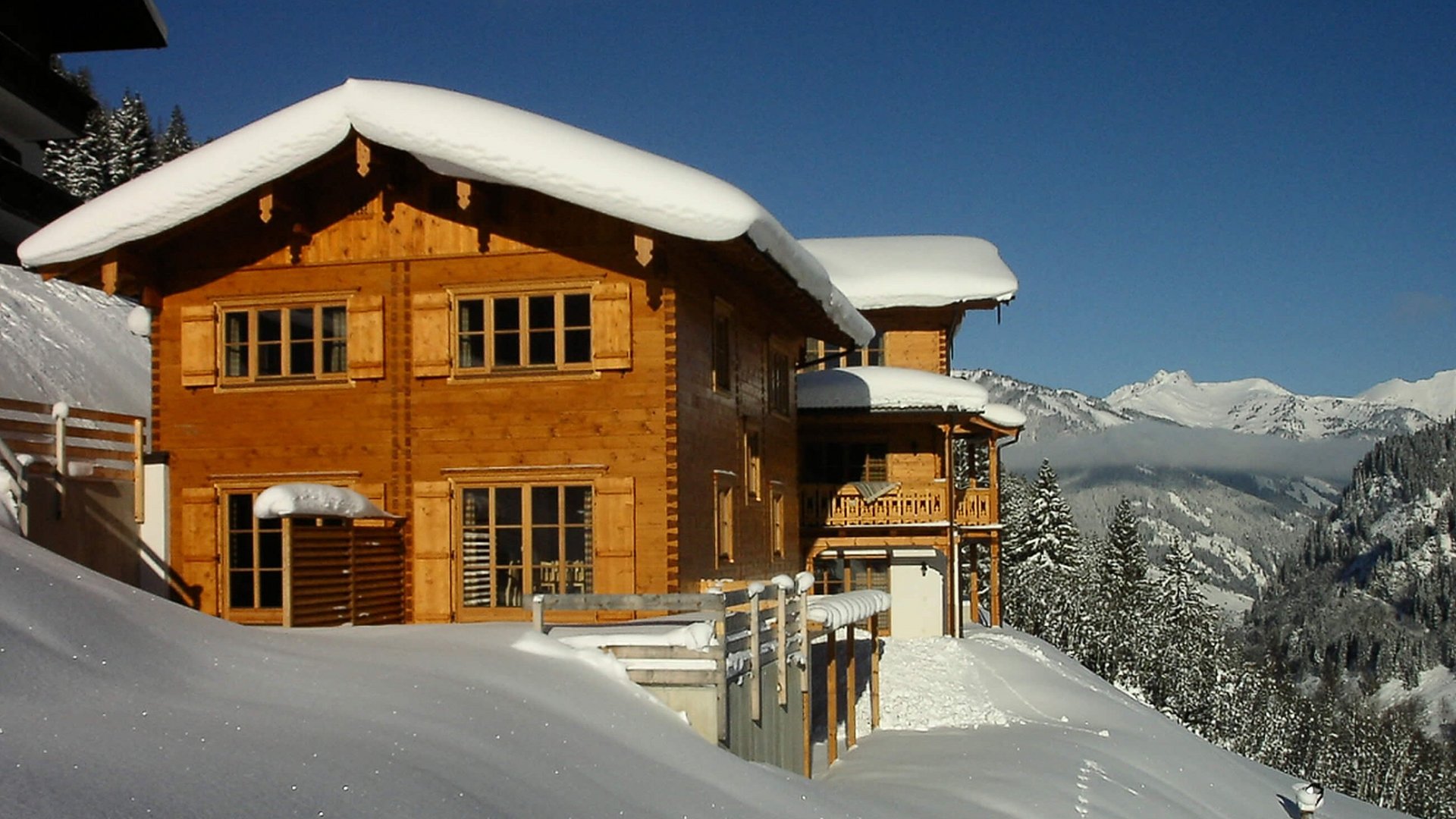 Wooden house covered in snow with mountains in the background