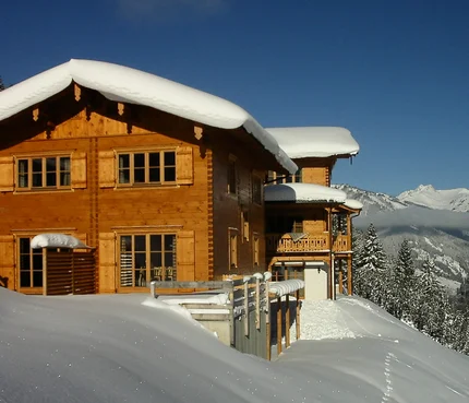 Holzhaus im Schnee mit Bergen im Hintergrund