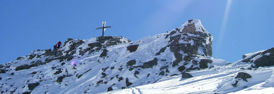 Hotel Eggerhof *** © Andreas Kleinwächter Schneebedeckter Berggipfel mit Gipfelkreuz und zwei Wanderern unter hellem Sonnenschein