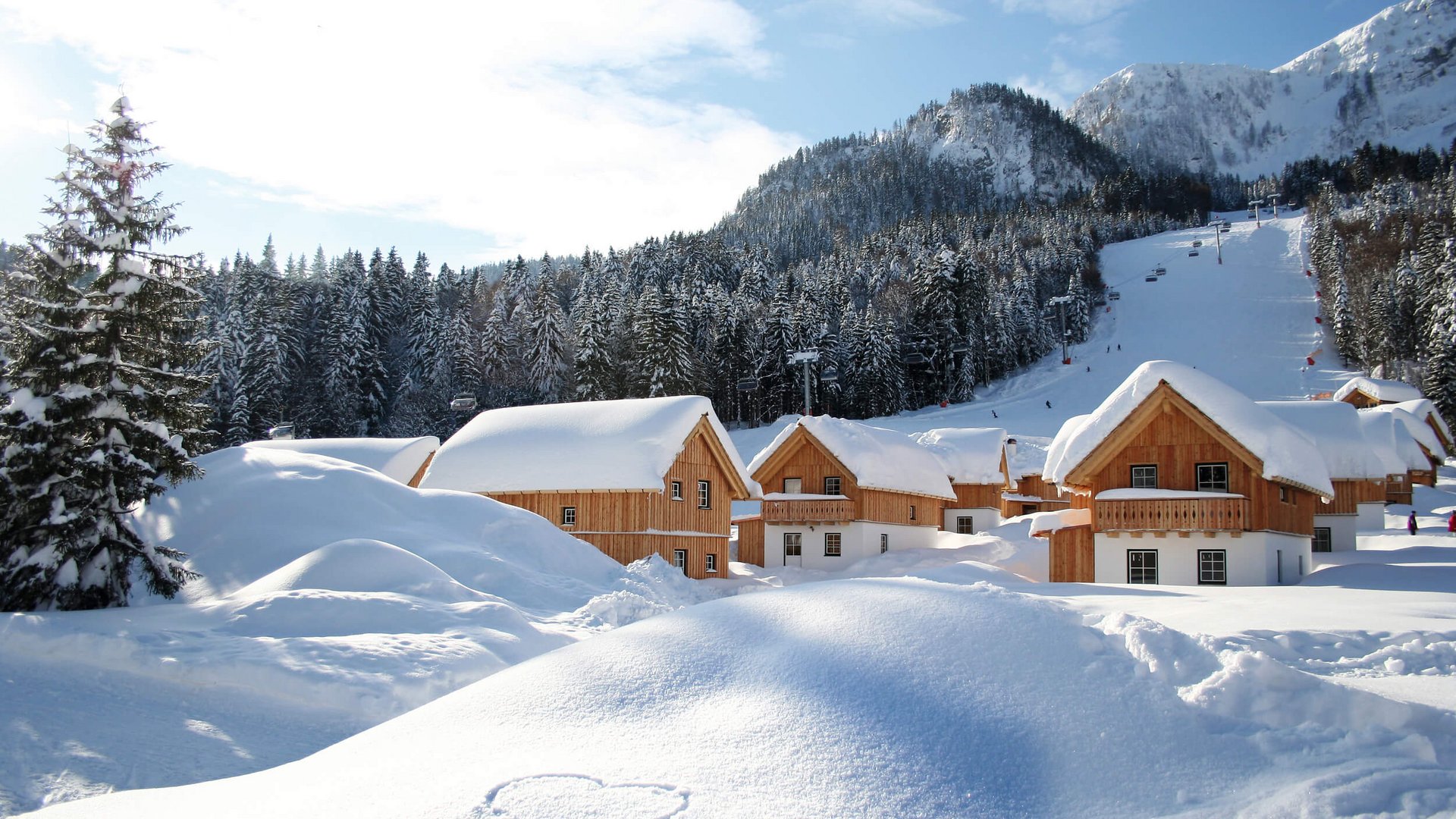 Snow-covered wooden houses near forested mountains and a ski slope