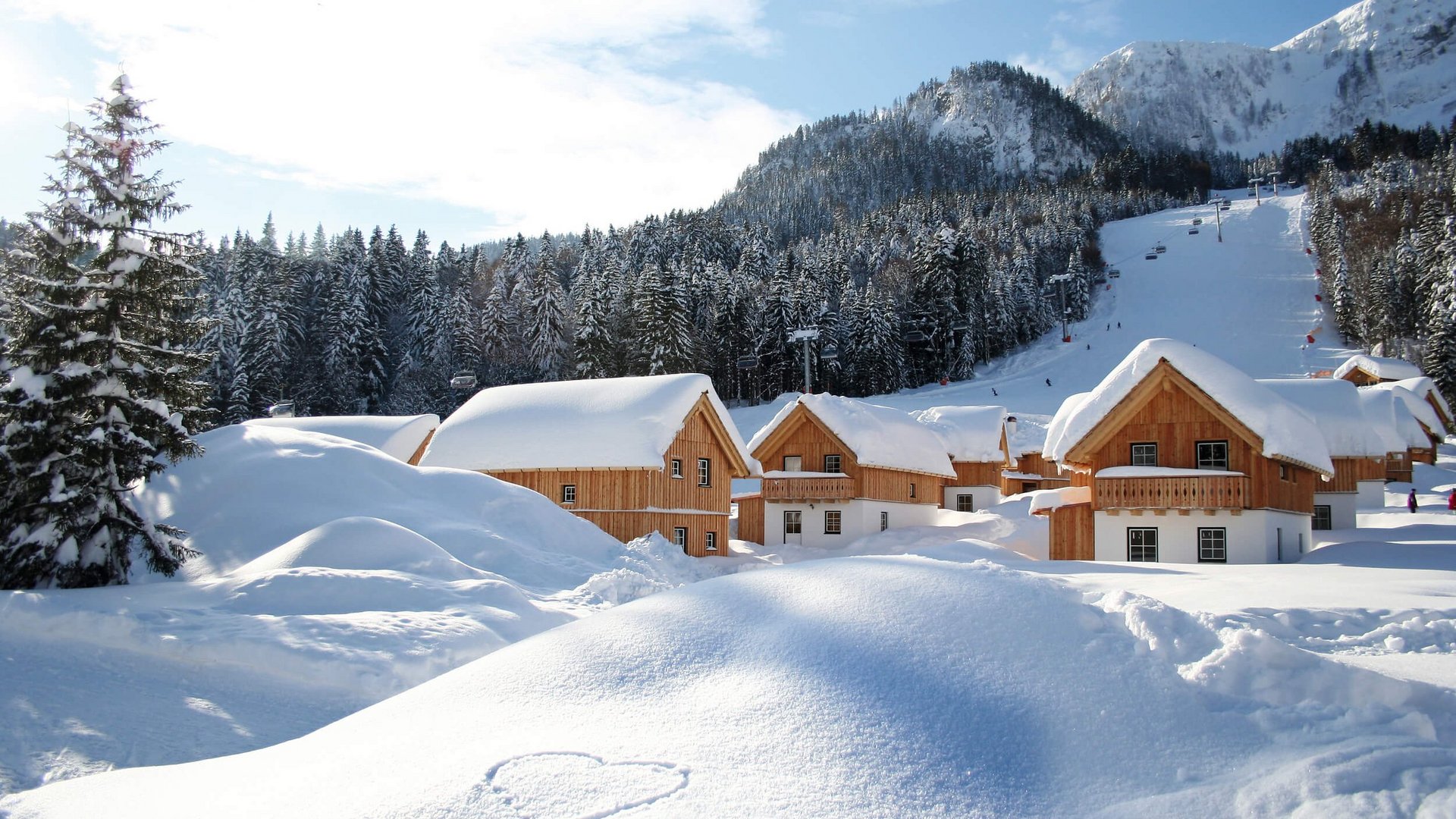 Snow-covered wooden houses near forested mountains and a ski slope