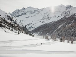 Zwei Skifahrer auf einer Spur in schneebedecktem Tal vor verschneiten Bergen
