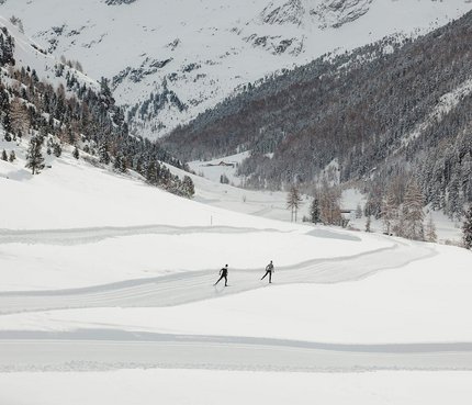 Zwei Skifahrer auf einer Spur in schneebedecktem Tal vor verschneiten Bergen