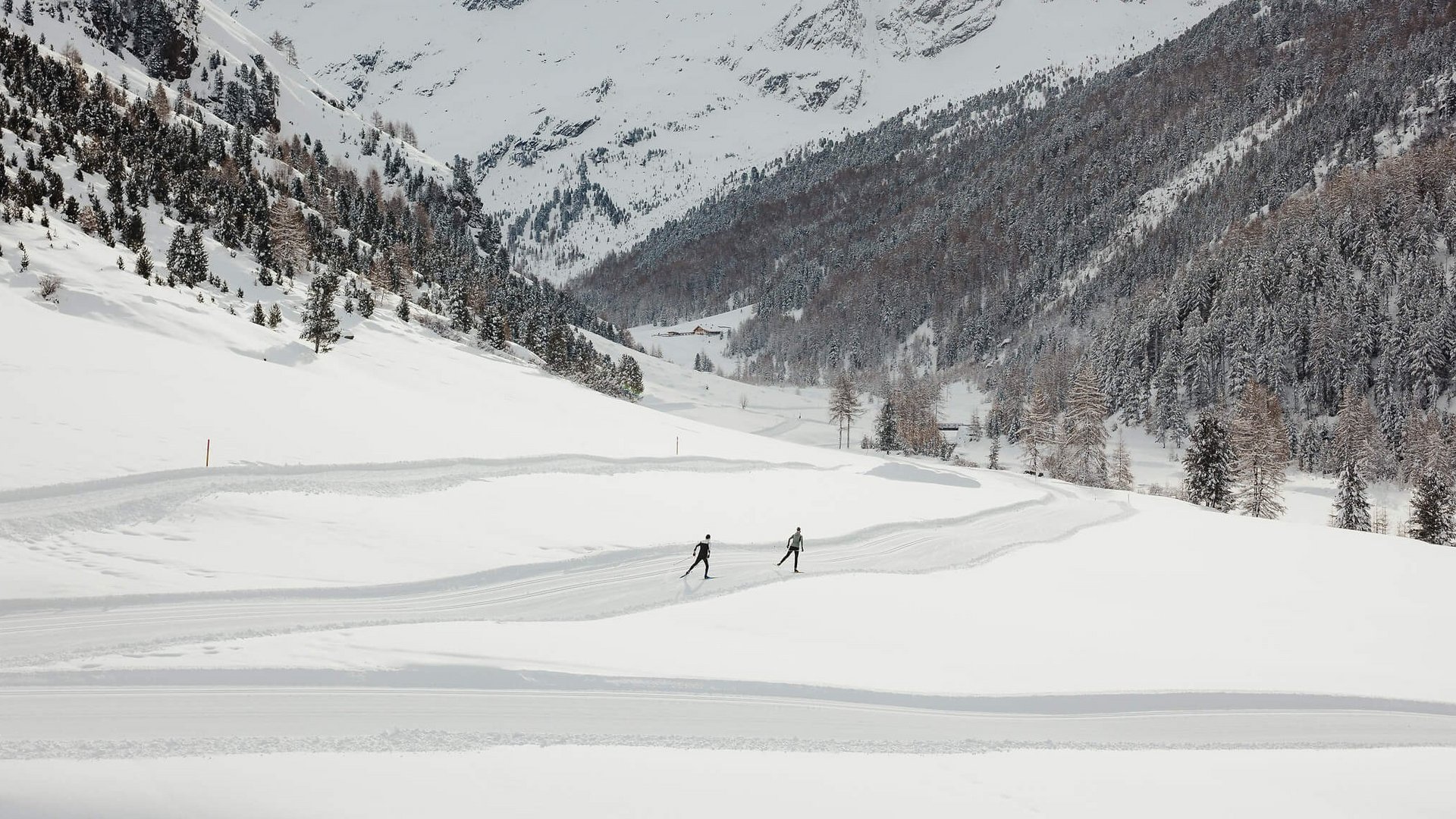Zwei Skifahrer auf einer Spur in schneebedecktem Tal vor verschneiten Bergen