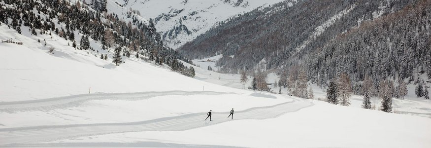 Zwei Skifahrer auf einer Spur in schneebedecktem Tal vor verschneiten Bergen