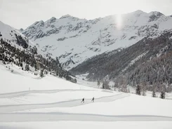 Zwei Skifahrer auf einer Spur in schneebedecktem Tal vor verschneiten Bergen