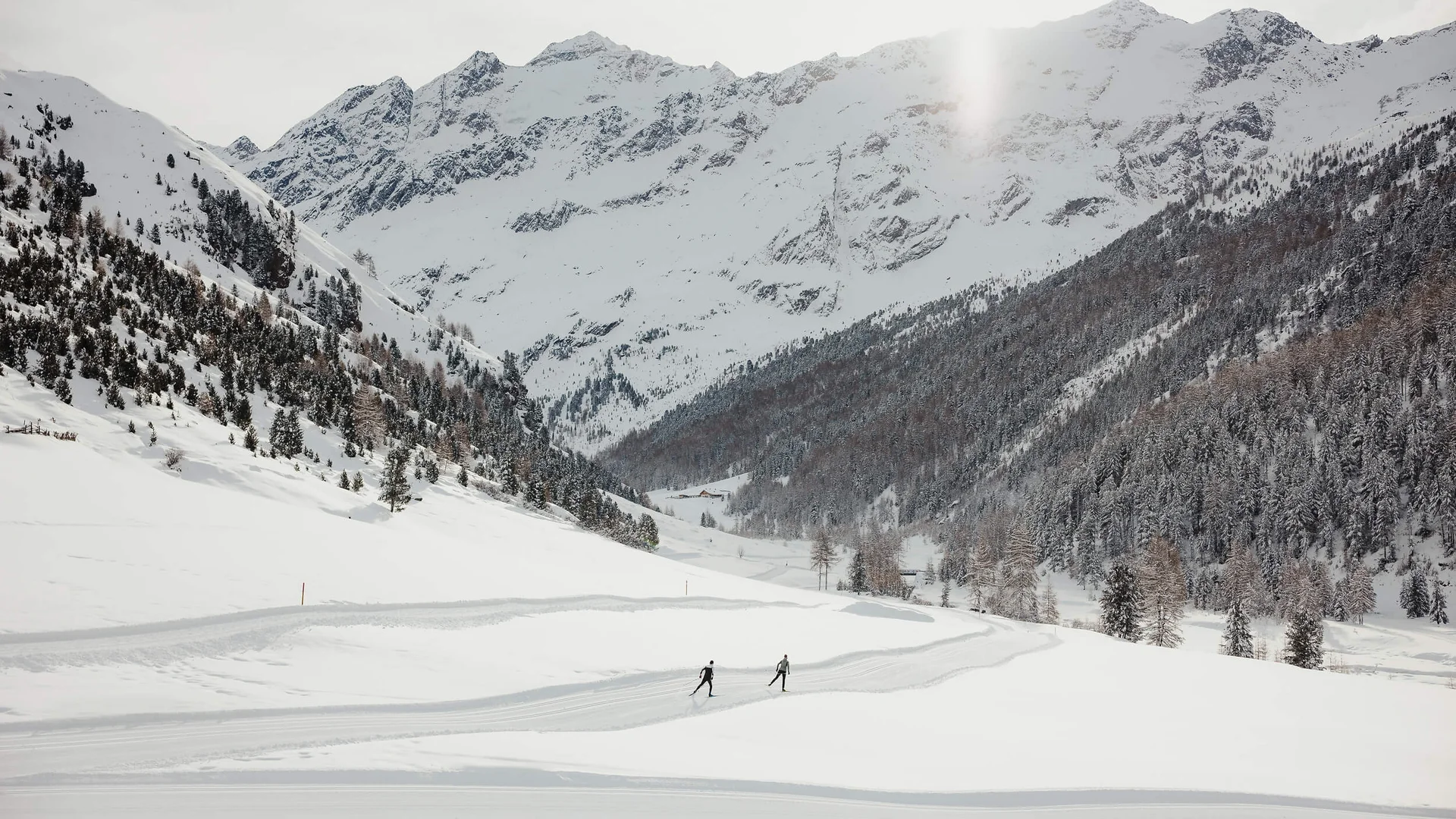 Zwei Skifahrer auf einer Spur in schneebedecktem Tal vor verschneiten Bergen