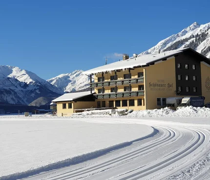 Schneebedecktes Hotel in den Alpen mit Loipenspuren im Vordergrund