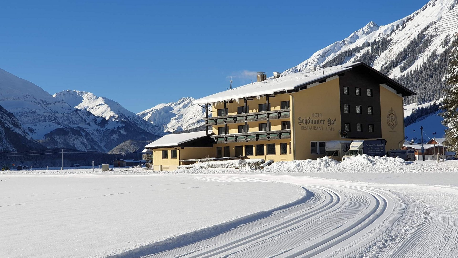 Snow-covered hotel in the Alps with ski tracks in front