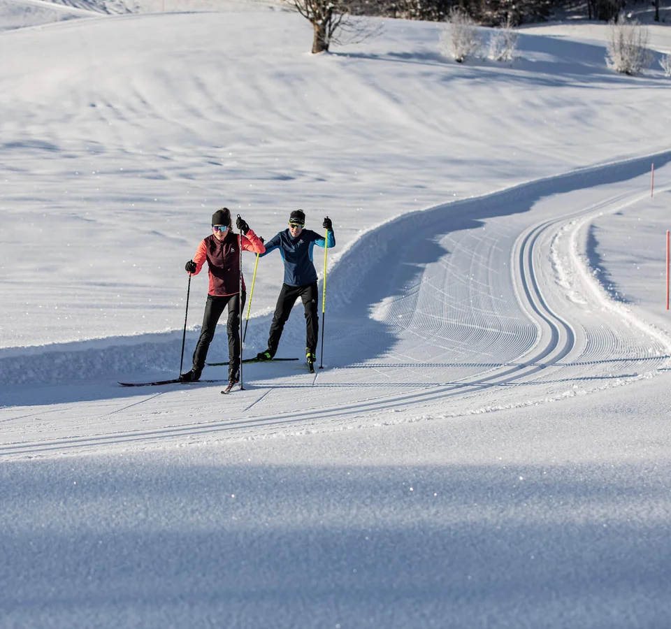 Two cross-country skiers on a groomed snowy trail in sunny weather
