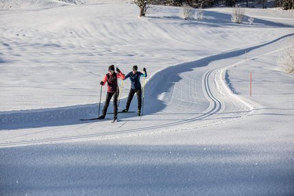 Zwei Langläufer auf einer präparierten Schneeloipe bei sonnigem Wetter