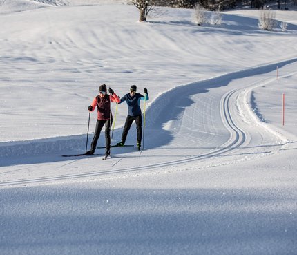 Zwei Langläufer auf einer präparierten Schneeloipe bei sonnigem Wetter