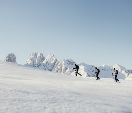 Drei Skitourengeher wandern im Schnee vor schneebedeckten Bergen