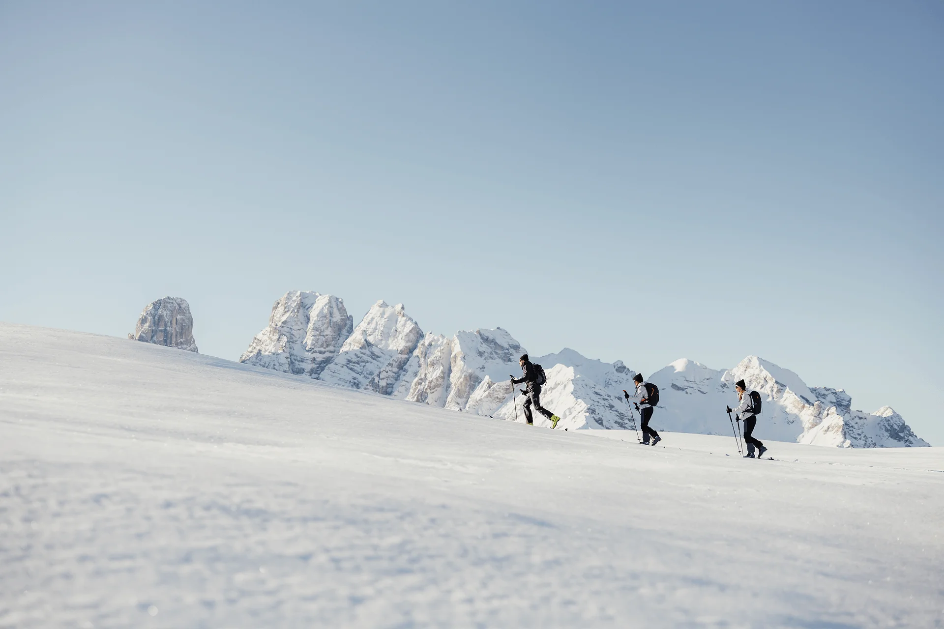 Three ski tourers hiking on snow in front of snowy mountains