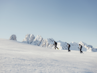 Three ski tourers hiking on snow in front of snowy mountains