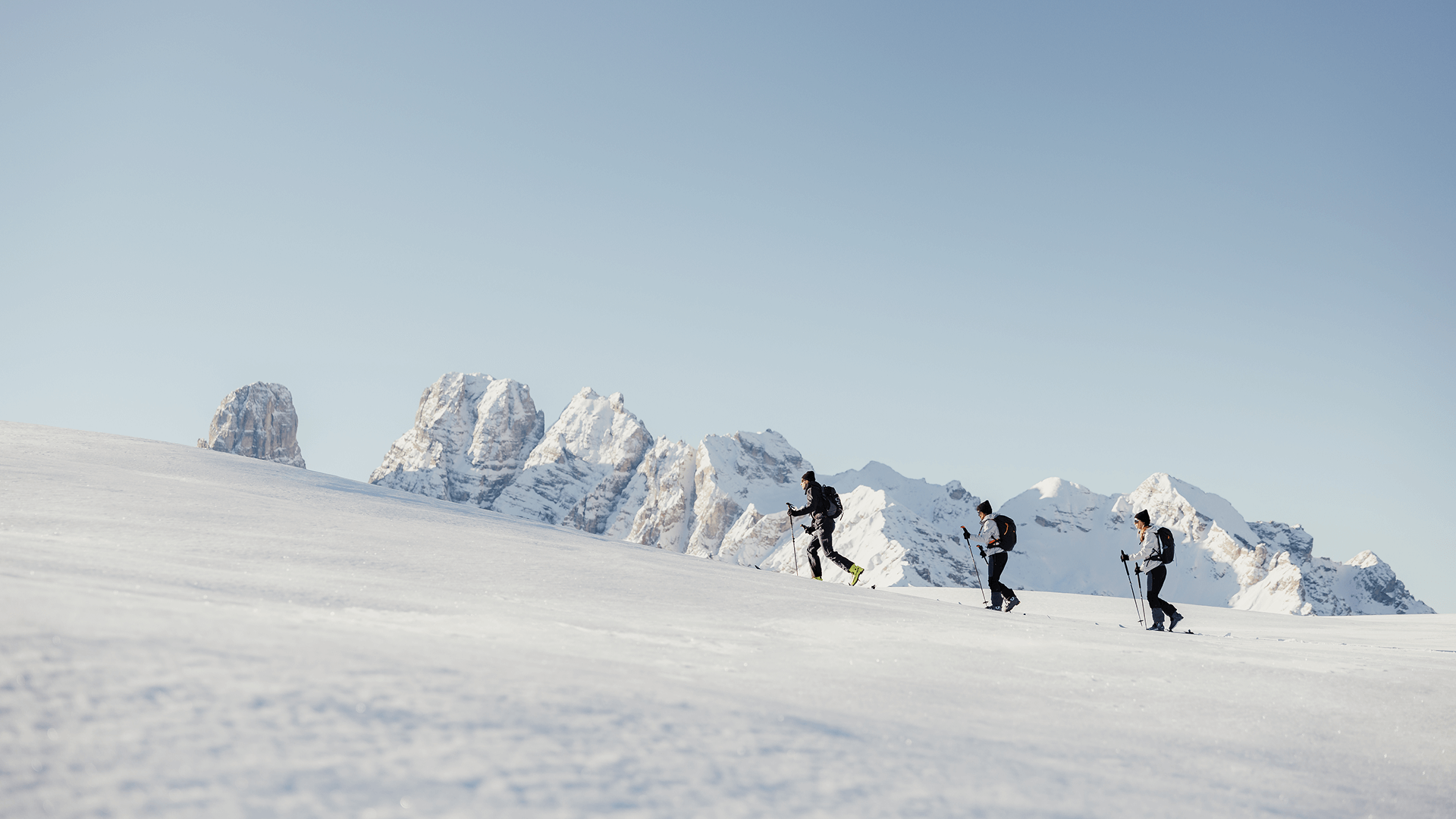 Drei Skitourengeher wandern im Schnee vor schneebedeckten Bergen