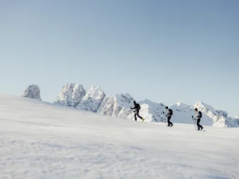 Three ski tourers hiking on snow in front of snowy mountains