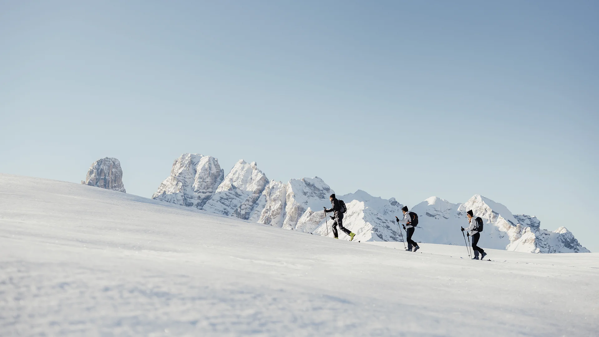 Drei Skitourengeher wandern im Schnee vor schneebedeckten Bergen