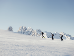 Drei Skitourengeher wandern im Schnee vor schneebedeckten Bergen