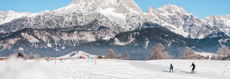 Zwei Skilangläufer auf Schneefeld vor schneebedeckten Bergen bei klarem Himmel