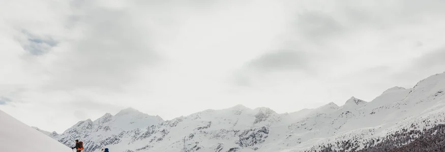 Zwei Skifahrer steigen einen schneebedeckten Hügel in den Bergen hinauf