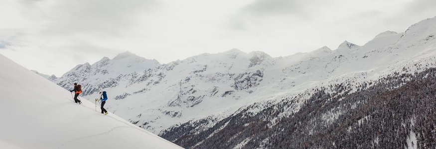 Zwei Skifahrer steigen einen schneebedeckten Hügel in den Bergen hinauf