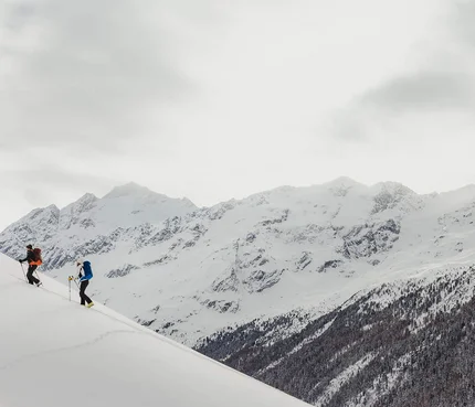 Zwei Skifahrer steigen einen schneebedeckten Hügel in den Bergen hinauf